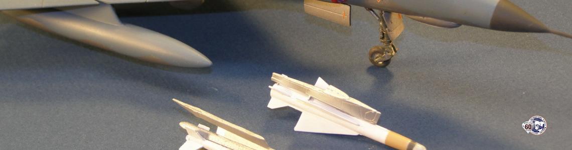 Assembled and painted missle attached to pylon next to same-scale aircraft.