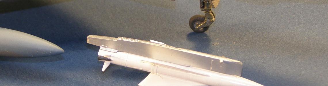 Assembled and painted missle attached to pylon next to same-scale aircraft.